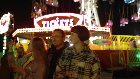 Three Excited Friends Discuss at Which Attraction To Go Near Ticket Office at Amusement Park alt