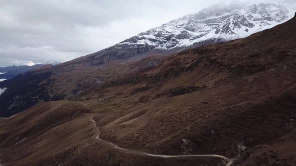 Aerial shot of brown barren mountain landscape criss-crossed by winding road and snowy hill in the b alt