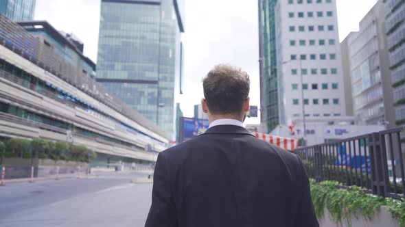 Attractive and Confident Businessman Walking Near Modern Office Building. alt