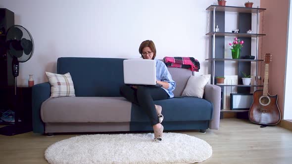 Mature Business Woman in Casual Clothes Is Sitting on the Couch and Working on a Laptop at Home