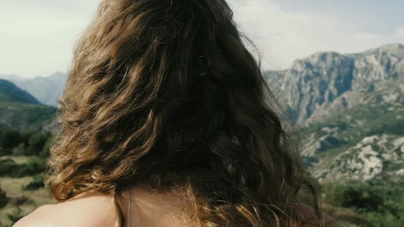 Young curly-haired woman standing on the background of the mountains alt