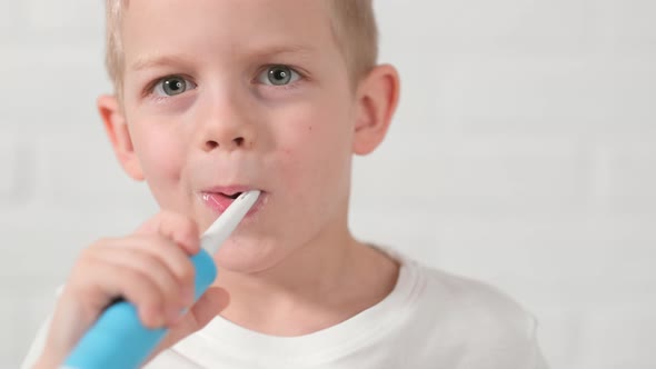 Portrait Happy Smiling Child Kid Boy Brushing Teeth with Electric Toothbrush on White Brick alt