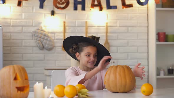 Cute Little Witch Sitting at Halloween Party With Jack Pumpkin Showing Thumbs-Up alt