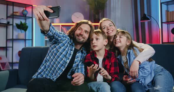 Family Sitting Together on the Sofa at Home in the Evening and Making Selfie on Smartphone alt