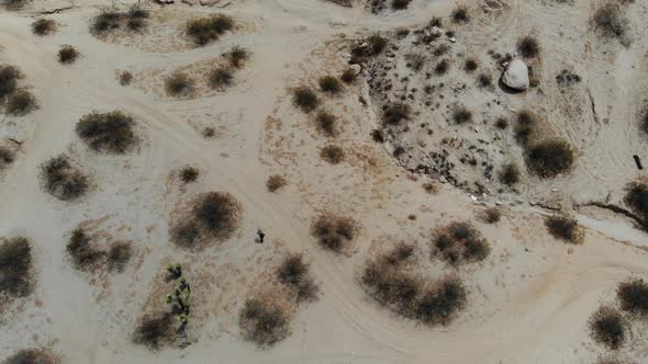 A Man leaves footprints in the desert as we watch him from a drone birds eye view walk through the b alt