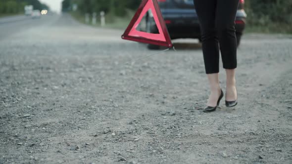 Low View of Woman with Broken Automobile Installing Red Triangle Sign on Road alt