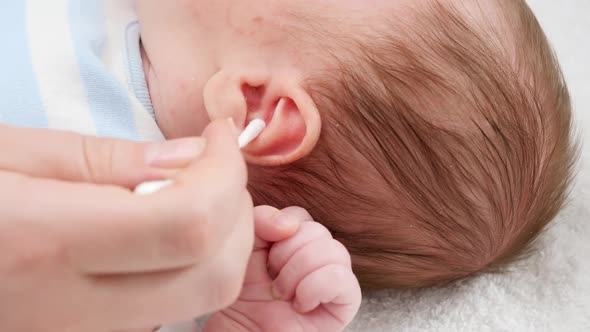 Closeup of Mother Using Cotton Swabs To Clean Little Baby's Ears From Ear Wax alt