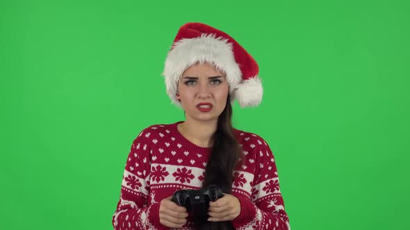 Portrait of Sweety Girl in Santa Claus Hat Is Playing a Video Game Using a Wireless Controller and alt