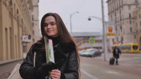 A Happy Brunette Girl in a Black Jacket Walks Through the City in Early Spring alt