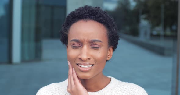 Close-up Portrait of African Mixed Race Ethnic Woman Standing Outdoors Feeling Toothache Bad alt