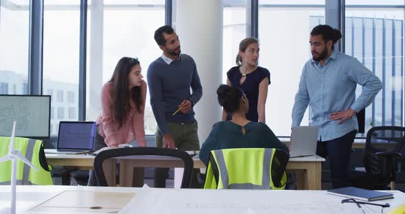 Diverse group of male and female architect colleagues gathered around a table and discussing alt