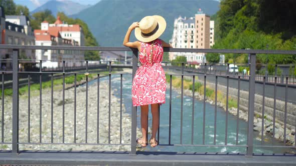 Little Girl at Hat on the Embankment of a Mountain River in a European City.