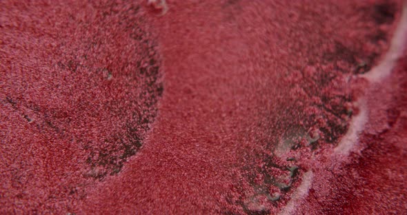 Water squirting onto a red sandlike surface. Particles get mixed with the water. alt