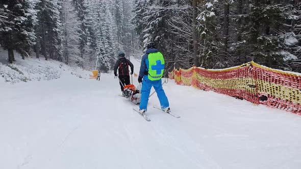 Mountain rescuers transporting an injured skier, going downhill after first aid