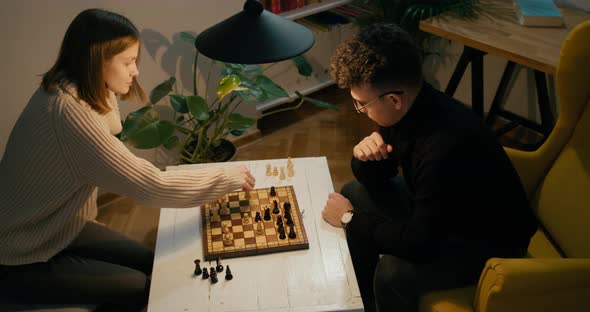 Man and Woman Play Chess Game at Home at Night