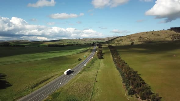 Drone Shot Of Truck And Cards Driving Down Country Highway Surrounded By Trees In Summer alt