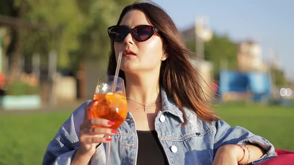 Female blogger takes pictures of a glass of cocktail in a cafe with her phone. alt