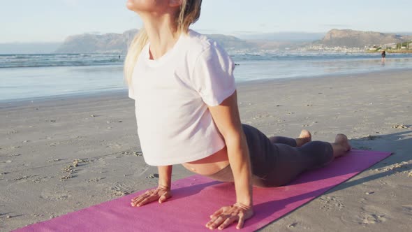Caucasian woman practicing yoga, stretching at the beach alt