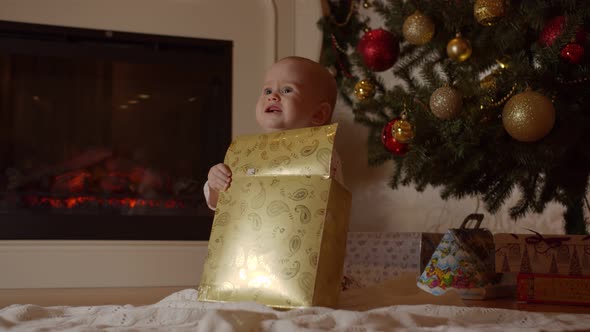 A Baby Is Unpacking a Christmas Present By the Tree