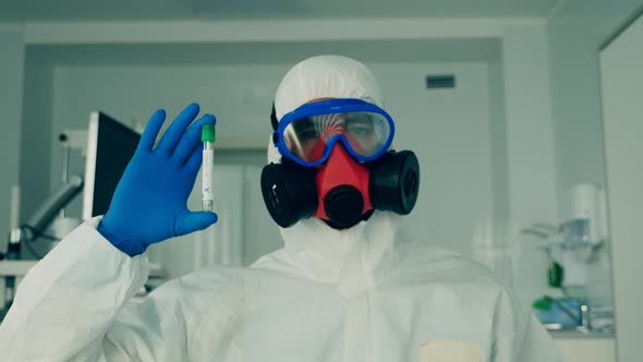 Person in Hazmat Holds a Tube with a Sample for Coronavirus alt