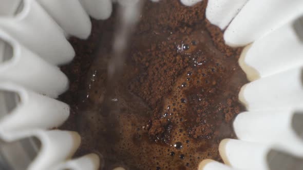 Hot water pour over into ground coffee beans close up slow motion alt
