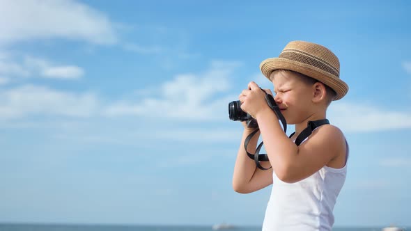 Happy Travel Child Boy in Hat Taking Photo of Seascape Using Camera at Blue Sky Background alt