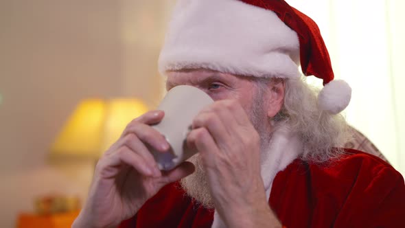 Closeup Face Bearded Old Santa Clause Enjoying Taste of Hot Milk Indoors in Living Room alt