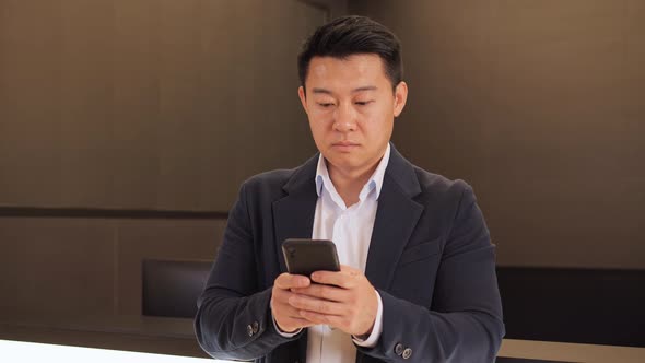 Focused Asian Businessman Using Smartphone Standing in Office alt