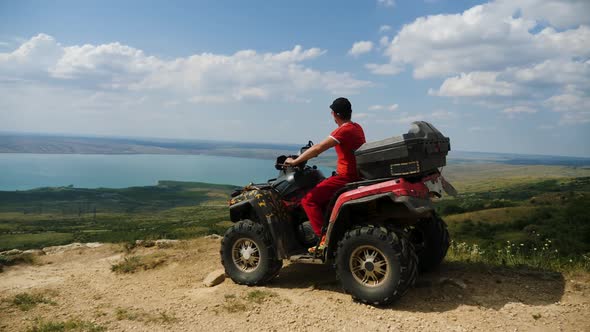 Man in a Black Cap and Red T-shirt on a Colored ATV Rides alt