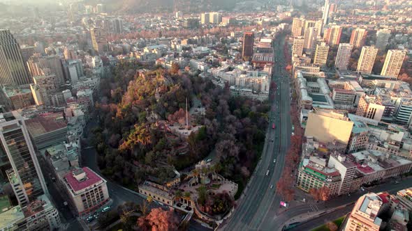 Aerial view dolly over Santa Lucia hill covered with autumnal trees, traffic in highway and Santiago alt