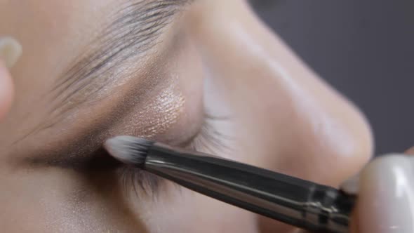Makeup Artist Applying Shiny Eye Shadows To Eyelid of Young Woman Eye Closeup