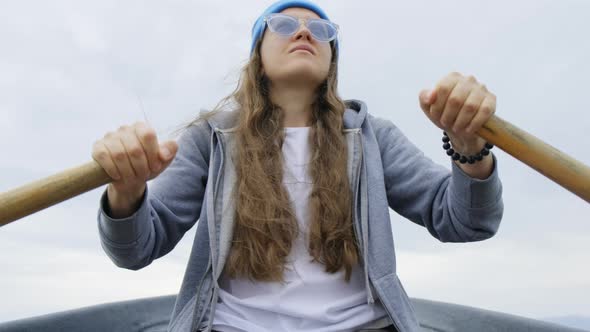 A Girl with Flowing Hair in a Blue Cap and Sunglasses Floats on a Rowing Boat alt