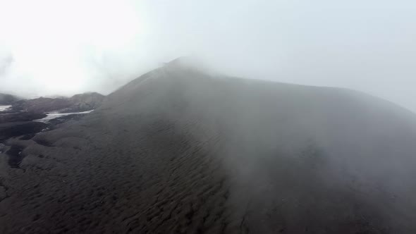 climbing a black snow-covered volcano in the clouds