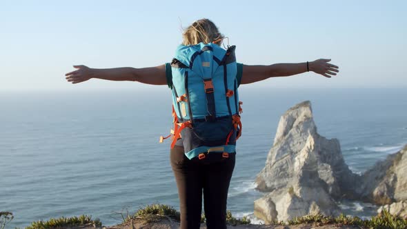 Excited Female Backpacker Standing at Rocky Cliff alt