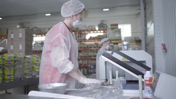 Side View of Confident Caucasian Woman in Face Mask and Uniform Packing Food Packaging Using alt