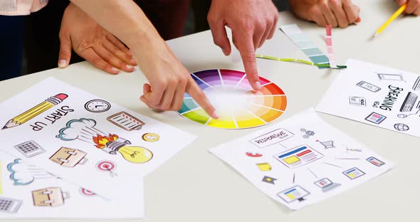 Graphic designers discussing over color swatch at desk alt