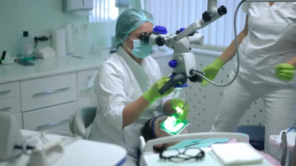 Concentrated Dentist Using Dental Microscope Examining Oral Cavity of Patient As Assistant Sitting alt