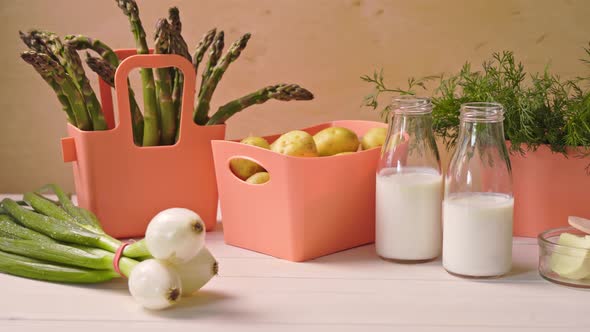 Spring Young Vegetables in Coral Containers and Bottles with Milk on Table