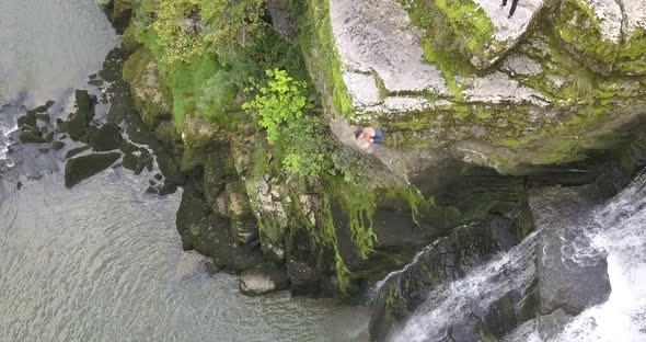 Young Cliff jumping athlete dives from a rock next to a waterfall in the Doubs river, Neuchatel, Swi alt