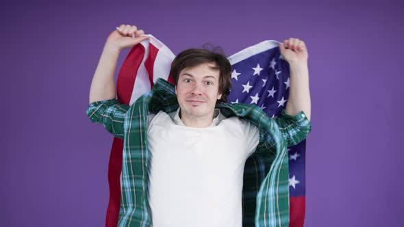 Young Emotional Man Waving American Flag and Shouting on Purple Background alt