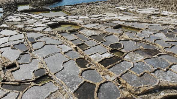 A slow, low-level aerial drone shot skims across the Salt Pans of Gozo island in Malta. alt