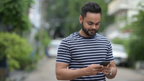 Young Happy Bearded Indian Man Using Phone Outdoors