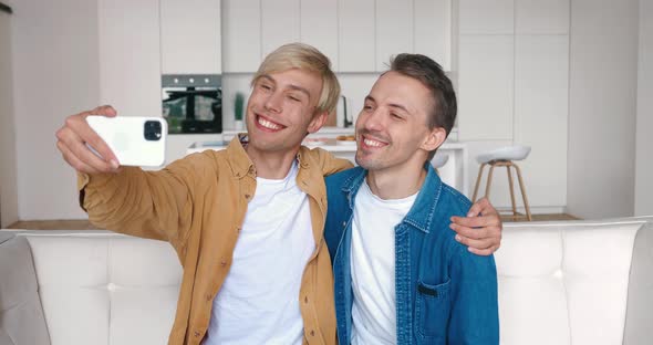 Homosexual Couple Hugging Looking at Smartphone Camera When Making Selfie Photos alt