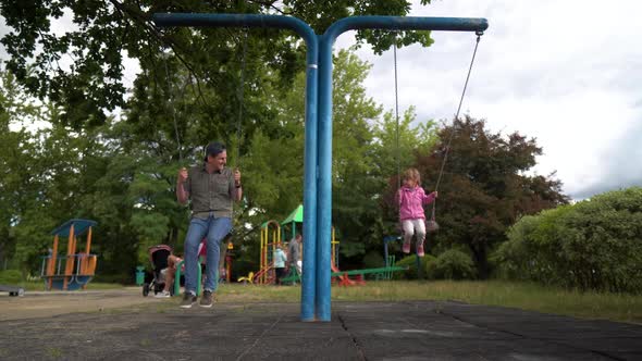 Happy Little Daughter is Having a Good Time on the Playground with Her Loving Father