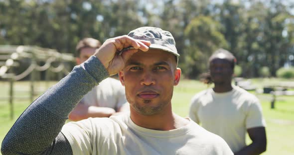Portrait of african american male soldier in cap smiling at obstacle course with two men behind him alt