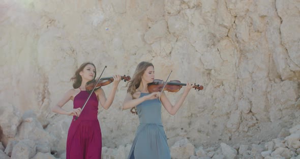 Two Pretty Ladies in Dresses Play Viola at Cliff Background in Sunny Summer alt