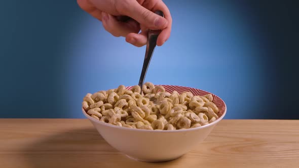 Man Hand Picks Up Crispy Corn Rings From White Plate Filled with Milk with Spoon alt