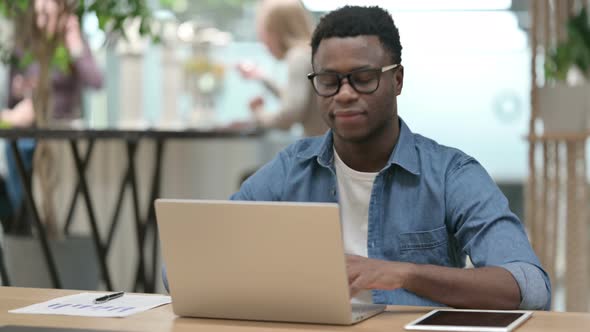 Young African Man Pointing at Camera While Working on Laptop alt