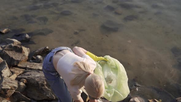 Young Woman Volunteer Collects Trash at the Lake