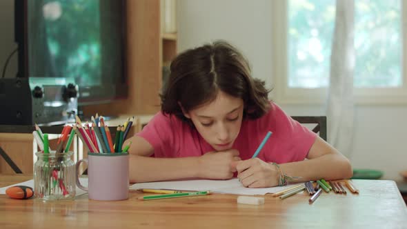 young girl sitting at the table drawing with colored pencils alt
